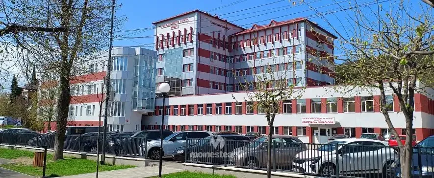 O clădire mare, albă cu dungi roșii, este înconjurată de copaci și are un parc de mașini în prim-plan.