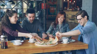 Patru persoane stau la o masă de lemn și împart o pizza pe o farfurie albă într-un local.