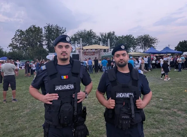 Doi bărbați în uniformă neagră cu veste tactice și berete stau în picioare pe un teren de iarbă în fața unei mulțimi.