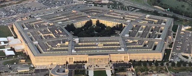 O vedere aeriană a unei clădiri pentagonale de culoare deschisă cu numeroase ferestre și curți interioare înconjurată de parcuri și zone de parcare.