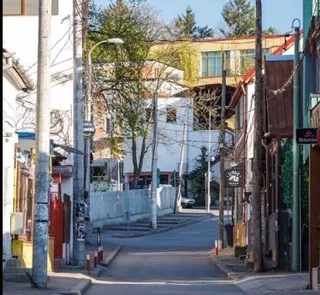 O stradă asfaltată este încadrată de clădiri, stâlpi de utilități și un gard gri pe partea stângă.