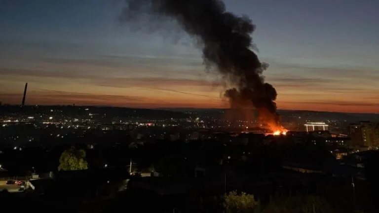 Un nor gros de fum negru se ridică deasupra unui oraș în timpul amurgului.