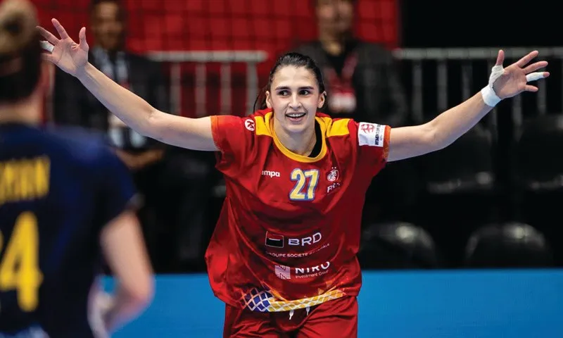O femeie cu mâinile întinse poartă un tricou roșu cu numărul 27 și este pe un teren de sport.
