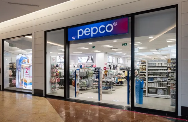Fațada unui magazin Pepco cu vitrine mari care expun rafturi cu diverse produse și haine în interiorul unei clădiri.