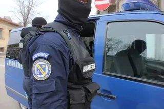 Un membru al jandarmiei în uniformă albastră și vestă tactică stă lângă un vehicul de serviciu de culoare albastră.