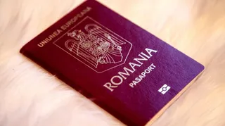 Un pașaport de culoare purpurie cu inscripțiile UNIUNEA EUROPEANĂ, ROMANIA și PASAPORT este așezat pe o suprafață albă și pufoasă.