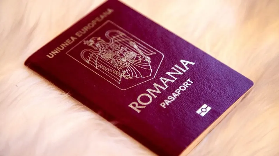 Un pașaport de culoare purpurie cu inscripțiile UNIUNEA EUROPEANĂ, ROMANIA și PASAPORT este așezat pe o suprafață albă și pufoasă.