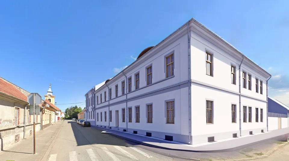 O clădire albă cu două etaje și ferestre dreptunghiulare este situată pe un colț de stradă sub un cer senin.