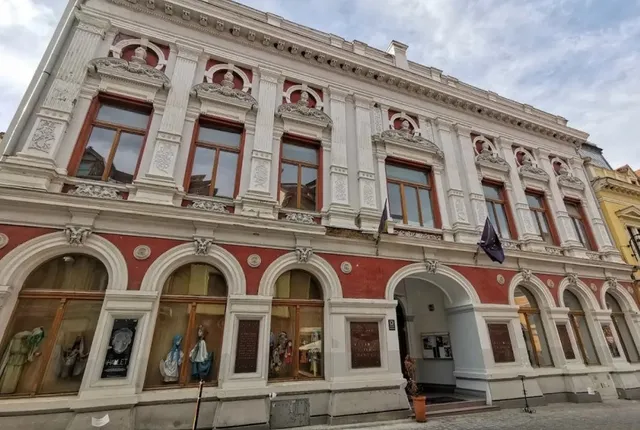 O clădire cu fațadă albă și roșie prezintă ferestre înalte, elemente decorative sculptate și vitrine de la nivelul străzii.