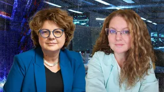 Două femei cu părul ondulat poartă sacouri, fiind poziționate în fața unui fundal cu ecrane și lumini albastre.