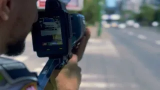 O persoană ține un aparat de măsurat viteza orientat spre o stradă cu mașini circulând în fundalul neclar.