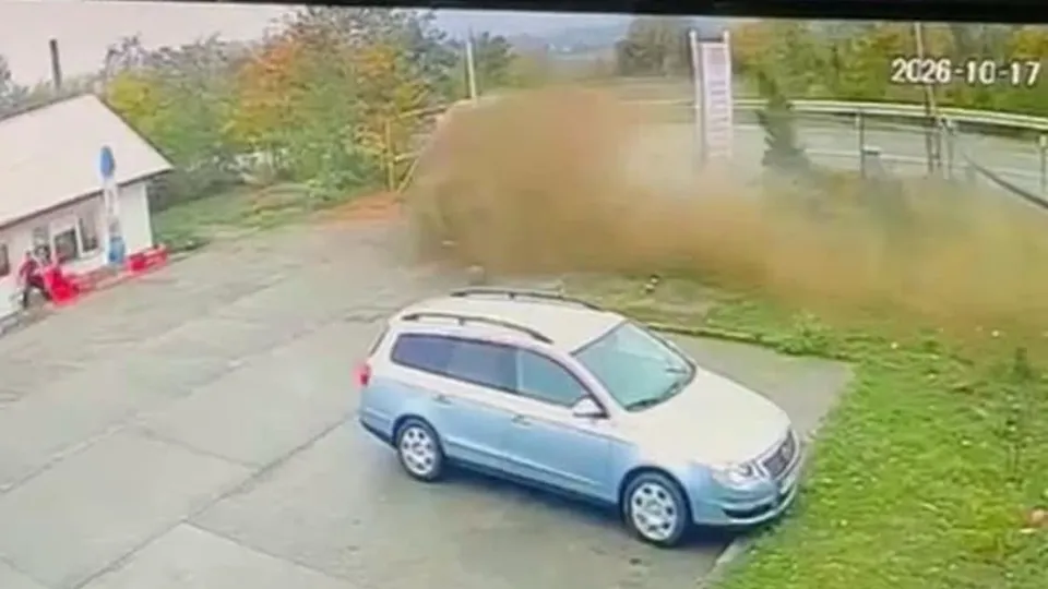 O mașină de culoare albastră este parcată pe o suprafață pavată lângă o zonă cu iarbă și un nor de praf ridicat în fundal.
