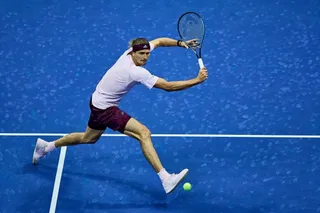 Un jucător de tenis cu bandană roșie și tricou alb lovește o minge pe un teren albastru.