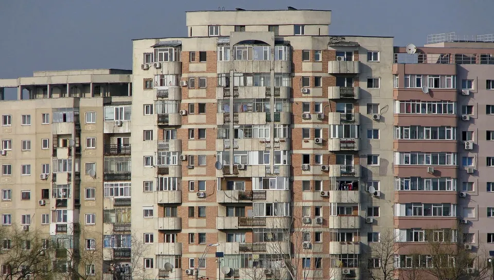 Blocuri de locuințe înalte cu ferestre, balcoane și unități de aer condiționat dispuse pe fațadele clădirilor sub un cer senin.