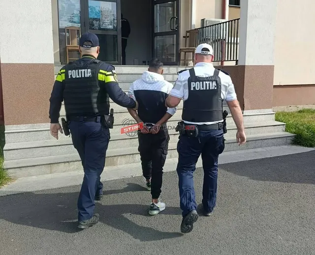 Trei polițiști în uniformă conduc un bărbat cu hanorac alb și pantaloni negri pe o scară în fața unei clădiri.