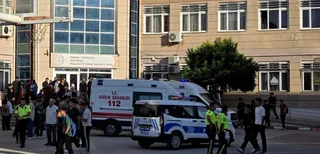 Mai mulți oameni stau lângă o clădire lângă două ambulanțe și o mașină de poliție parcată pe o stradă.