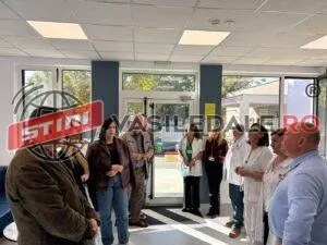 Un grup de persoane stă în picioare într-o încăpere cu uși de sticlă și ferestre mari, purtând haine casual și halate albe.