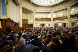 Oamenii stau așezați la mese în interiorul unei săli de conferințe circulare cu coloane albe și balcone din lemn.