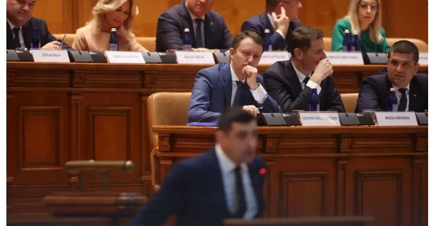 Bărbați în costume și femei în haine elegante stau așezați la mese de lemn în interiorul unei săli cu panouri de lemn.