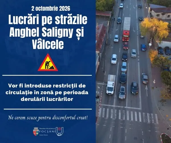 O vedere de sus a unui drum cu mașini circulând pe benzi marcate și un afiș albastru cu text și un simbol de lucrări rutiere.