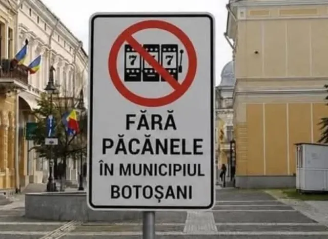 Un semn alb cu un cerc roșu tăiat care conține o pictogramă de aparat de jocuri de noroc și textul scris în litere negre.