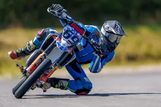 Un motociclist într-o combinație albastră și neagră înclină o motocicletă pe o pistă asfaltată.
