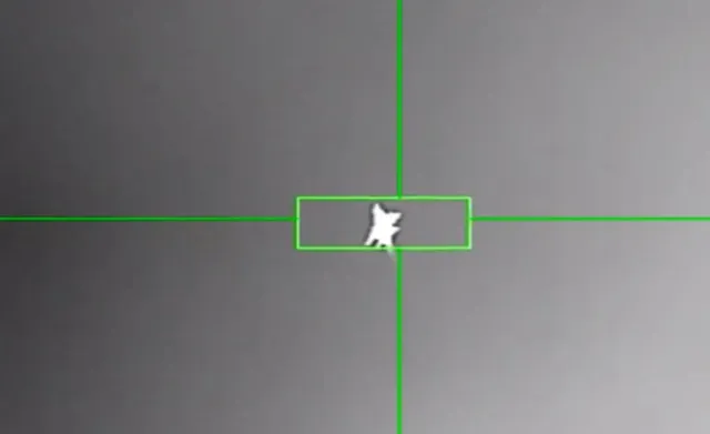 O siluetă albă de avion este vizibilă în centrul unei reticule verzi pe un fundal gri.