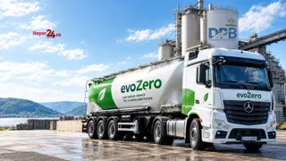 Un camion alb cu marcaje verzi și textul evoZero este parcat pe un teren deschis lângă silozuri de depozitare sub un cer înzăpezit.