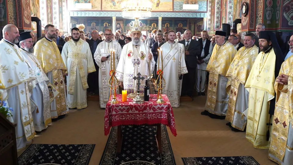 Un grup de bărbați îmbrăcați în robe liturgice albe și aurii stau în interiorul unei biserici în jurul unei mese acoperite cu un șervețel roșu.