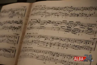 Pagini deschise ale unei partituri muzicale cu note scrise pe rânduri de pentagramă sub o lumină caldă.