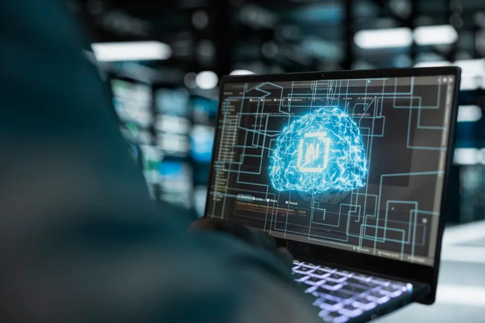 Un laptop afișează o ilustrație digitală a unui creier format din conexiuni luminoase pe un fundal negru cu linii de circuit.