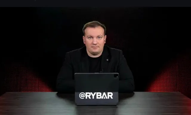 Un bărbat cu părul scurt și haine negre stă la o masă în fața unui ecran negru, având un dispozitiv cu textul @RYBAR în față.