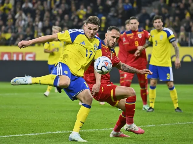 Un jucător în echipament galben și albastru lovește o minge de fotbal pe un teren verde în fața unor jucători în echipament roșu și mulțime.