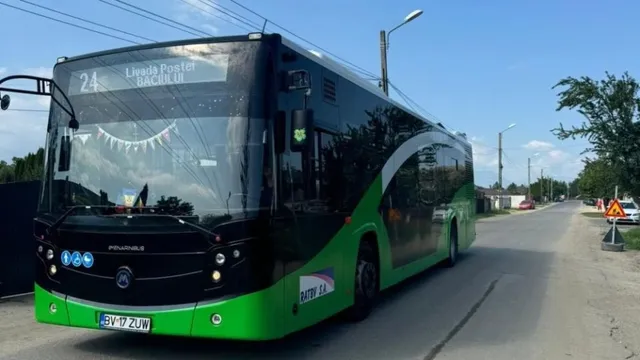 Un autobuz verde și negru cu numărul 24 afișat pe partea frontală circulă pe un drum asfaltat sub un cer senin.
