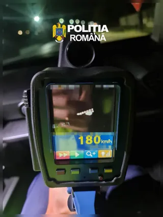 Un dispozitiv electronic de măsurare afișează cifra 180 km/h pe un ecran luminos într-un mediu întunecat.