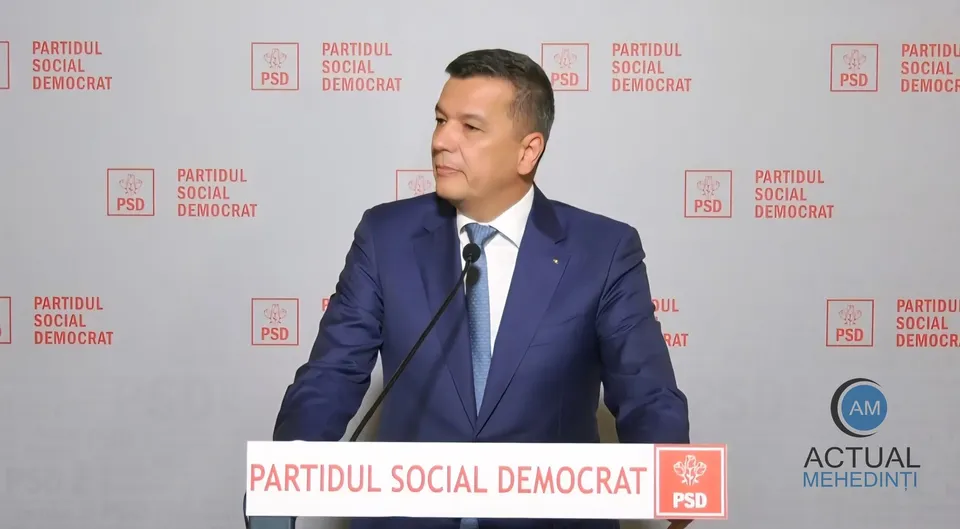 Un bărbat cu păr scurt și costum albastru cu cămașă albă și cravată deschizătoare stă în fața unui fundal cu logourile PSD repetate.