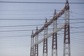 Mai multe turnuri metalice de înaltă tensiune susțin numeroase cabluri electrice întinse pe un cer deschis.