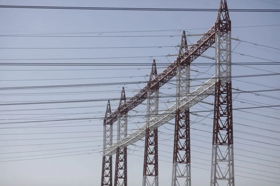 Mai multe turnuri metalice de înaltă tensiune susțin numeroase cabluri electrice întinse pe un cer deschis.