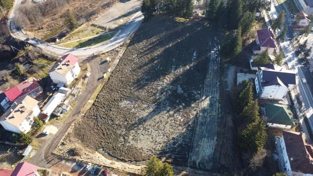 Vedere aeriană a unui teren dreptunghiular împrejit de arbori, clădiri și drumuri, cu o porțiune de pământ tulburat și urme de excavare.