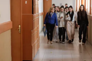 Un grup de elevi și o femeie merg pe un coridor de școală lângă dulapuri de lemn.