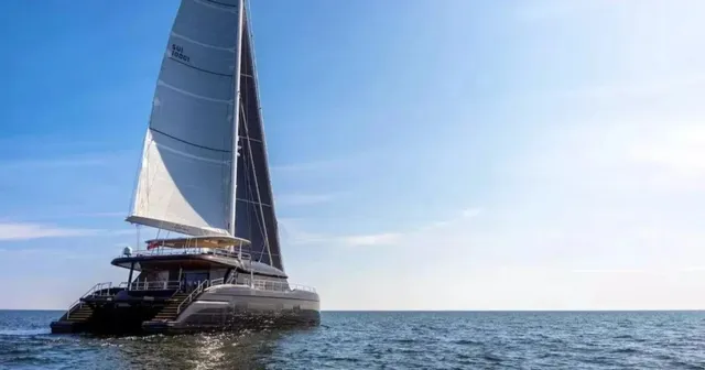 Un catamaran cu catarm mare și nave albe navighează pe o suprafață de apă sub un cer senin.