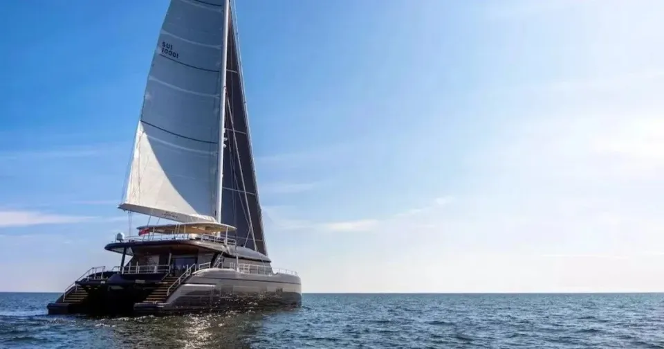 Un catamaran cu catarm mare și nave albe navighează pe o suprafață de apă sub un cer senin.