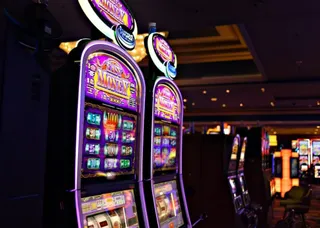 Mai multe aparate de joc de tip slot machine sunt aliniate într-o încăpere întunecată cu lumini colorate.