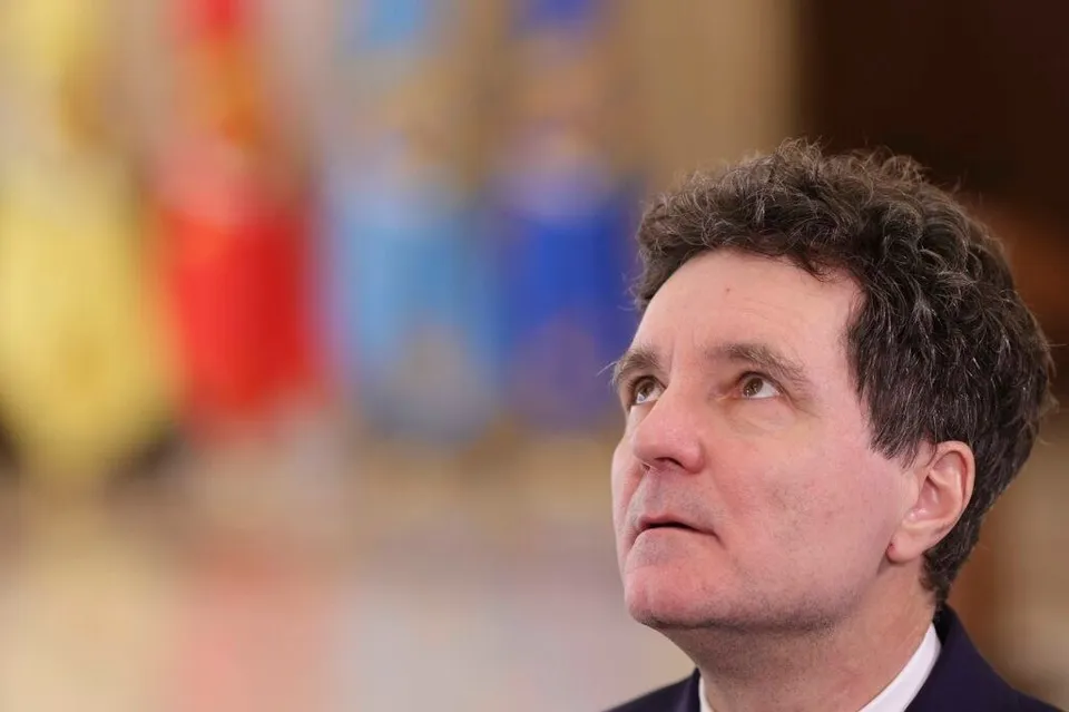 Un bărbat cu părul scurt și creț privește în sus, având un fundal colorat și neclar.