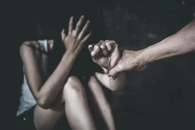 O persoană stă ghemuită într-un spațiu întunecat, în timp ce o mână masculină îi apucă încheietura brațului.