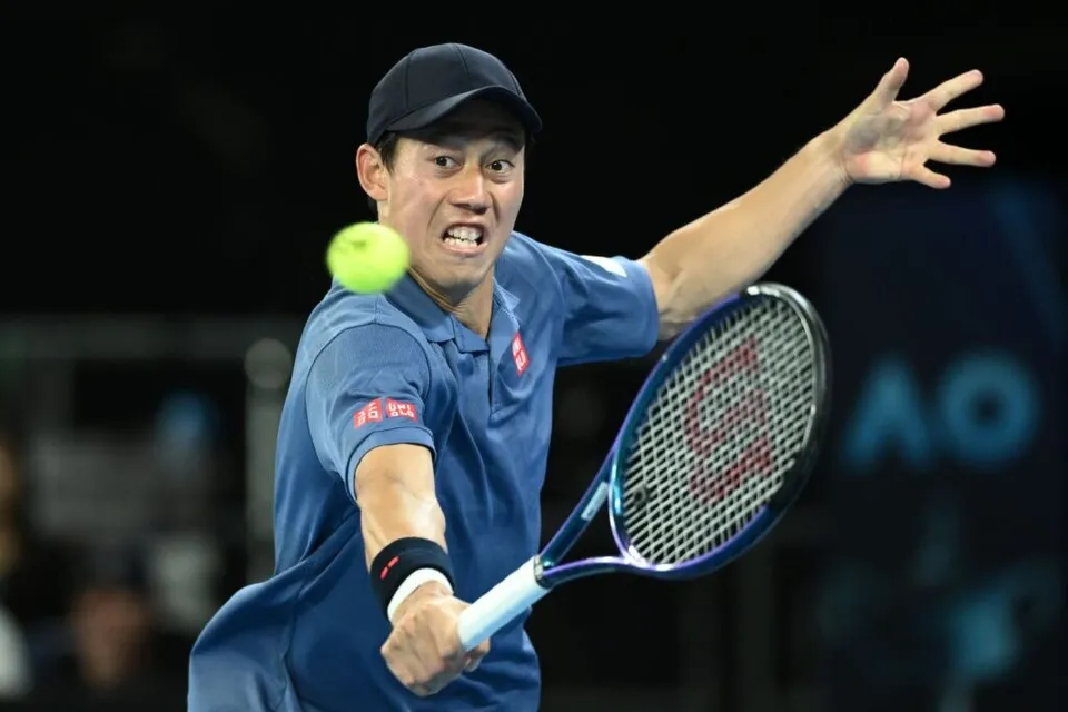 Un bărbat cu șapcă și tricou albastru lovește o minge de tenis cu o racletă într-o poziție de mișcare.