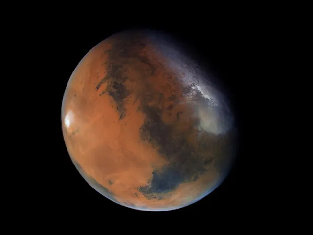 O imagine a planetei Marte, cu nuanțe de portocaliu și zone întunecate, pe un fundal negru.