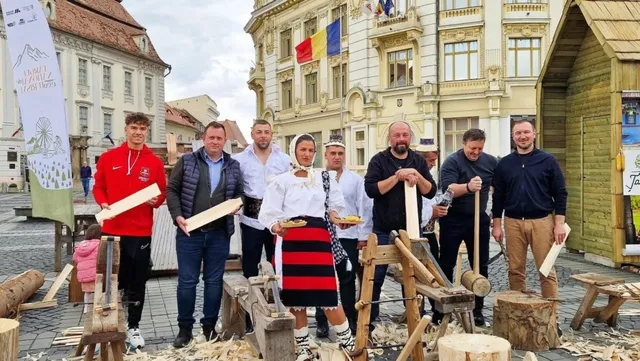 Un grup de oameni stă într-o piață pavată lângă construcții din lemn și resturi de așchii, în fața unor clădiri cu steaguri.