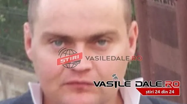 Un bărbat cu părul scurt și părți albe pe gulerul cămășii privește spre cameră.