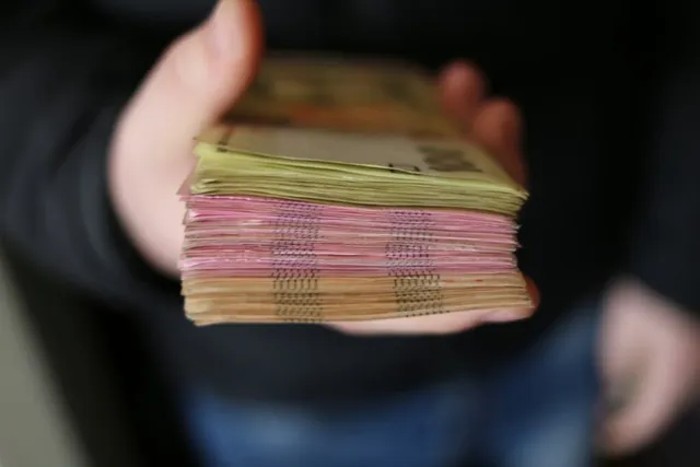 O persoană ține în palmă un teanc gros de bancnote colorate.